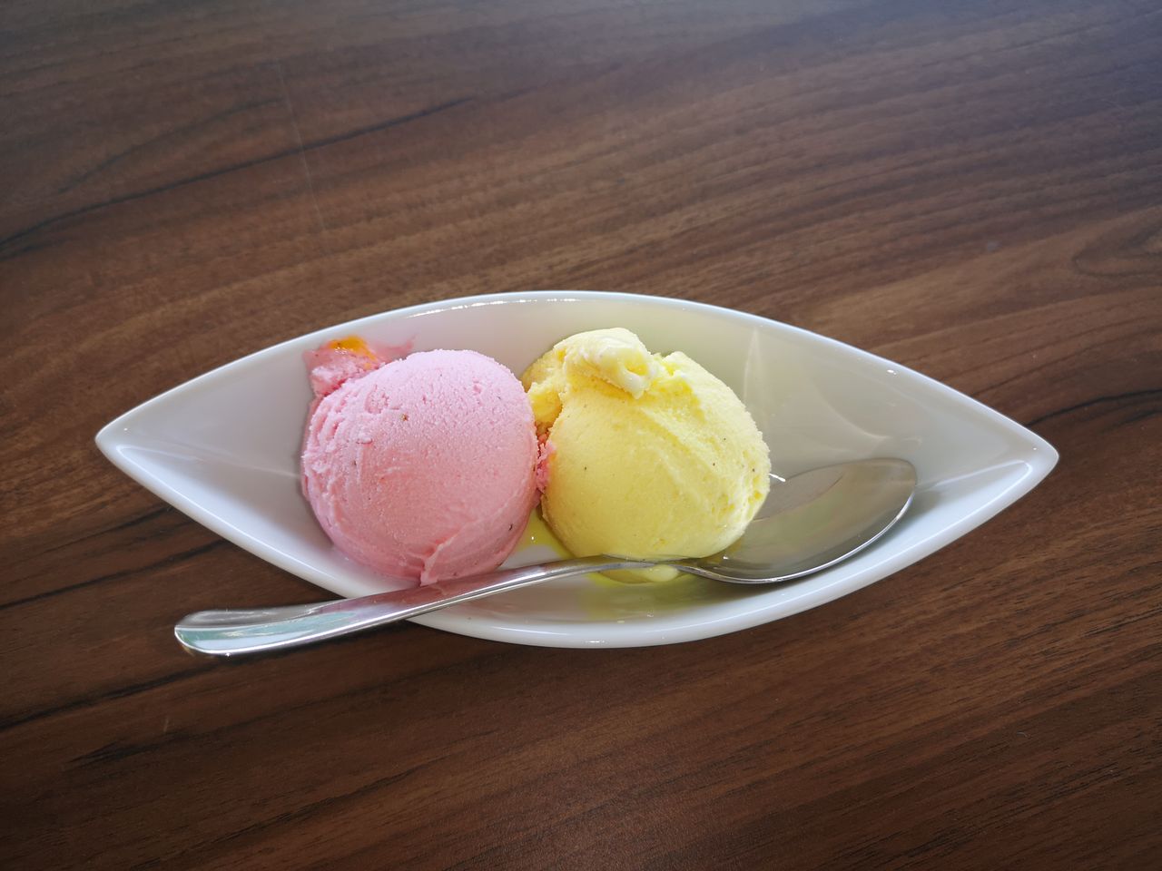 Blog Delicious strawberry and lemon ice cream scoops served in a white bowl with a spoon on wooden table.