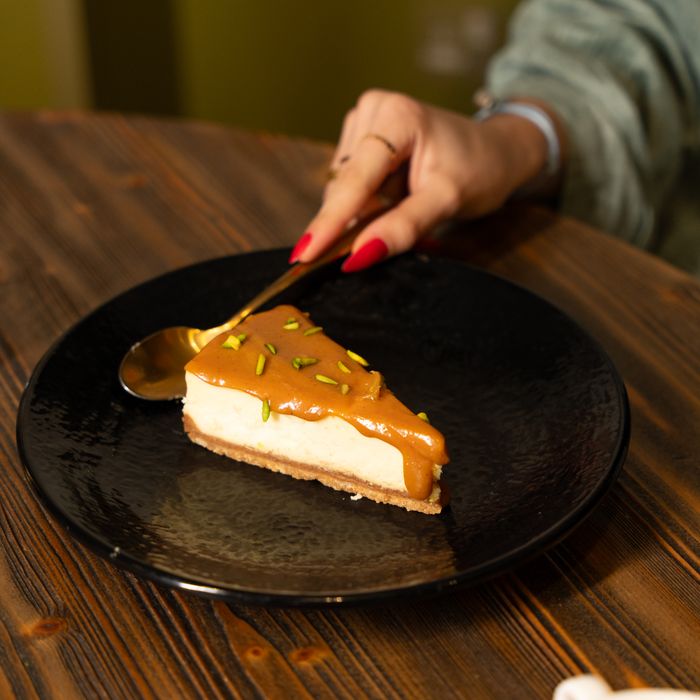 A person enjoys a delicious slice of caramel-topped cheesecake on a black plate.